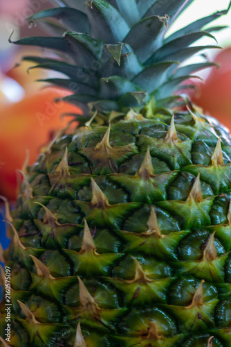 A large tropical pineapple fruit. The outside green skin is waxy. The multiple fruit has side shoots or suckers. The top has lush green leaves with spiky tips. The produce is edible on the inside.