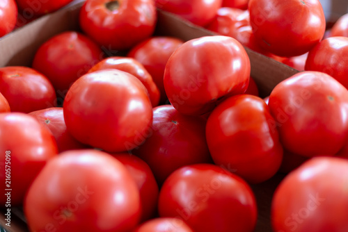 A harvest of large fresh organic tomatoes stockpiled in a crop bunch for sale at a farmers' market.The raw tomatoes are stacked, exposing the bright red color of the vegetables with smooth shiny skin.