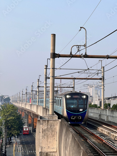 Bild auf Leinwand A modern electric commuter train traveling along an elevated railway in a busy city environment, approaching on parallel tracks beneath a network of overhead electrical wires and supporting poles