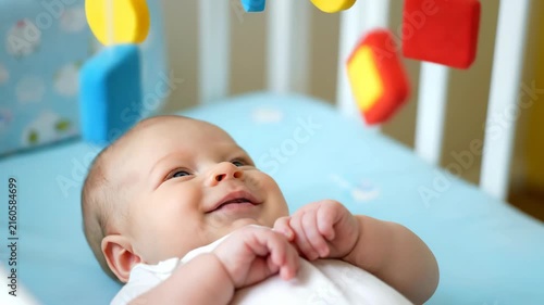 Newborn baby lying on soft bed with colorful toy hanging