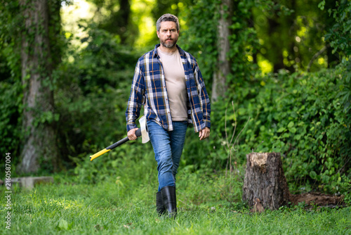 Foto Mature Lumberjack with serious face holds axe in the forest