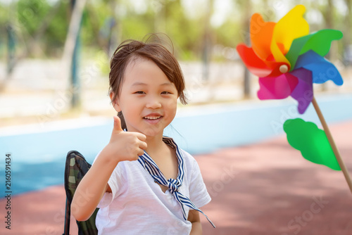 Fotografie Cheerful young girl giving a thumbs up sign while sitting outdoors with a blurred pinwheel background
