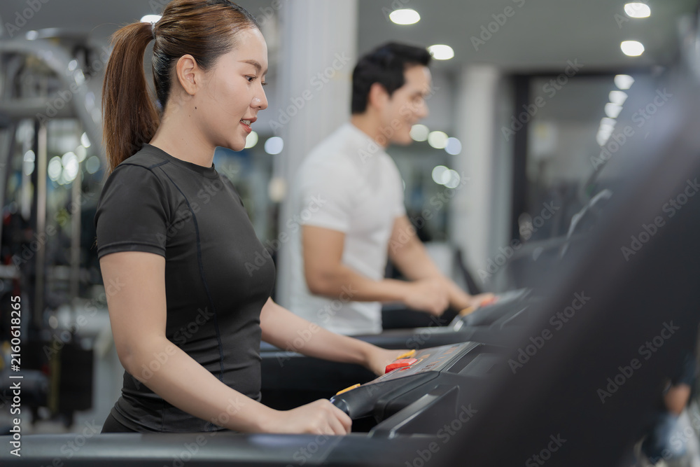 Fototapeta premium Asian man pressing touchscreen display on treadmill with personal trainer or gym partner in background