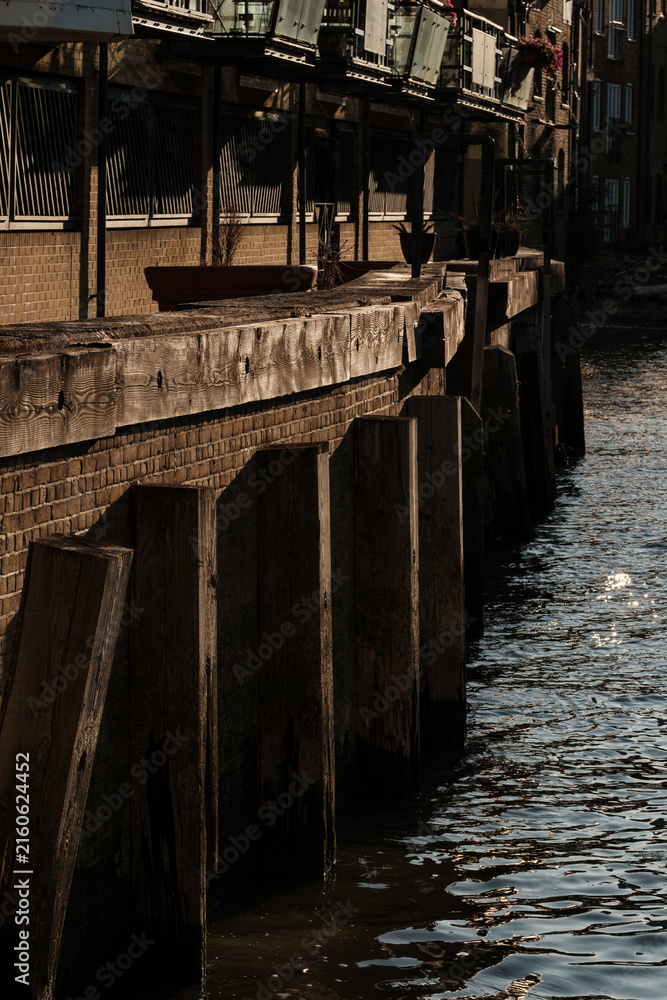 Fototapeta premium Wooden river embankment with brick wall and buildings