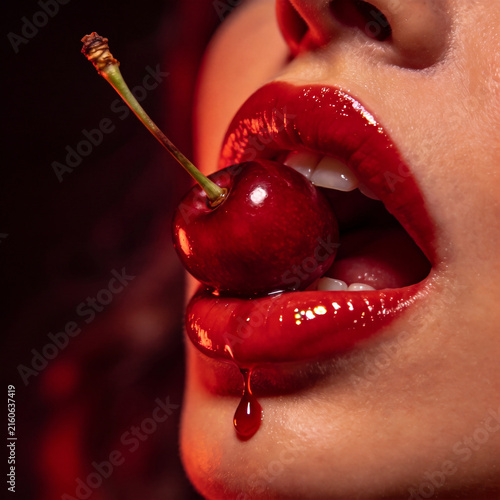 Vibrant Close-up of Glossy Red Lips Holding a Juicy Cherry, with a Syrupy Drop of Juice Dripping Down