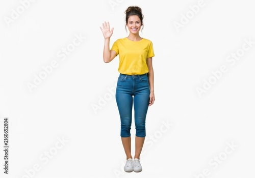Young woman wearing yellow t-shirt waving hello with a friendly smiling face isolated on white background