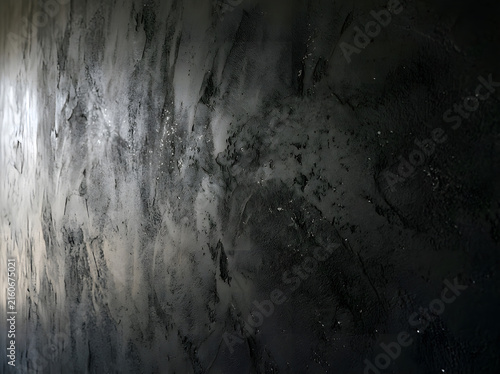 Close-up of textured matte black plaster wall with subtle cracks and uneven surface for modern design