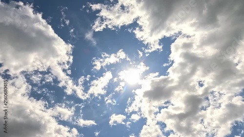 timelapse of fluffy white clouds floating across a blue sky, the bright sun shining through changing gaps as the clouds slowly merge, expand and gradually change shape throughout the frame.