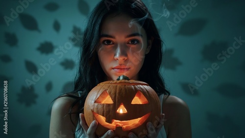 Young woman holding glowing carved pumpkin in dark halloween setting