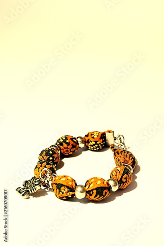 Digitally stylized photo illustration of a handmade ethnic bracelet with orange batik fabric beads and a silver charm. Perfect for fashion, cultural crafts, and artisan jewelry design concepts.