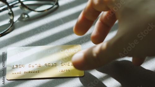 Financial decision, hand picking up gold credit card under Venetian blinds sunlight for payment concept.