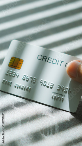 Financial decision, hand picking up silver credit card under Venetian blinds sunlight for payment concept. business credit debt concept.