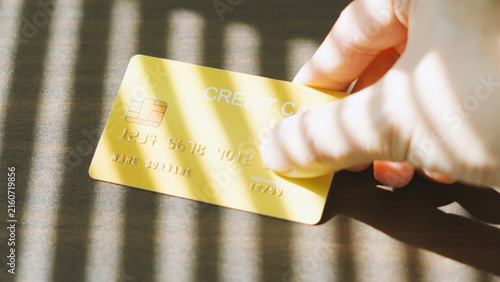 Secure online payment, hand holding golden credit card on wooden table under window blind shadow. Financial Debt Business concept.