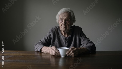 Elderly Woman Holding White Cup While Sitting at Wooden Table