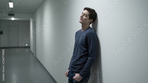 Young Man in Blue Shirt Leaning Against Wall in Empty Hallway