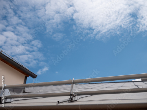 Metal snow guards on a standing seam roof under blue sky, showing roof safety, snow retention, modern construction and winter protection with copy space.
