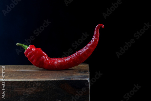 Red chili pepper on wood block against black background