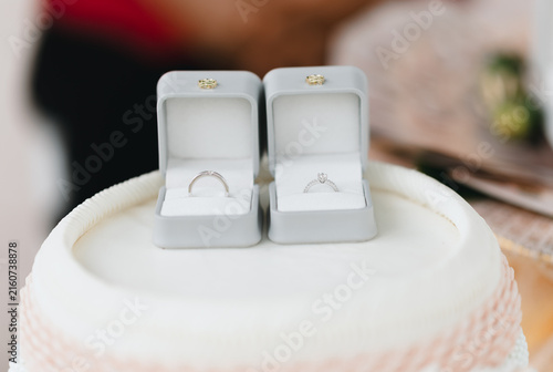 Quadro su tela Elegant Wedding Rings on a Table with Wedding Cake and Candle, Romantic Rings on