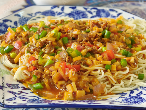 Homemade noodles with meat sauce and vegetables on blue and white porcelain plate