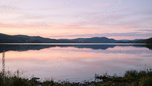 Reflective mountain lake mirroring soft pink and blue sunset sky