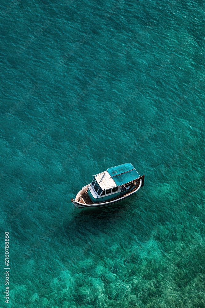 Fototapeta premium Leisure boat floating on clear turquoise coastal water aerial view