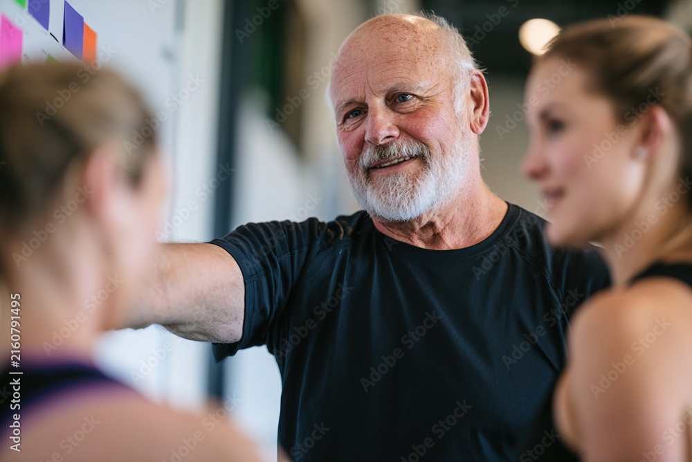 Fototapeta premium Coach explaining color - coded exercise plan to clients in modern training studio