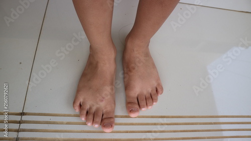 фотографія Child's bare feet standing on a light tiled floor with textured strips, showing
