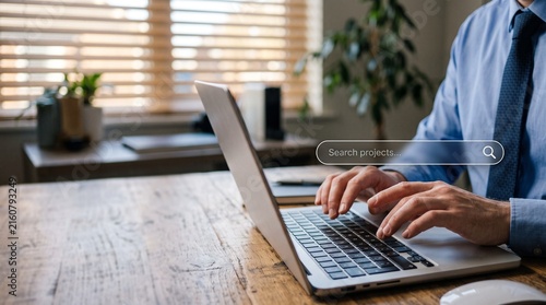 Online Search in Office: A businessman in a formal shirt and tie diligently types on a laptop, engaging in an online search on his desk. The scene conveys productivity and information gathering.