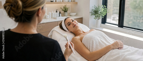 Facial treatment woman relaxing on spa bed during skincare consultation with therapist in bright modern wellness salon, expressing calm trust and comfort