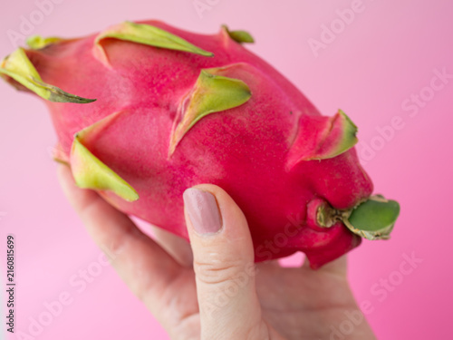 Fotografie Close-up of ripe red dragon fruit held in a hand against pink background