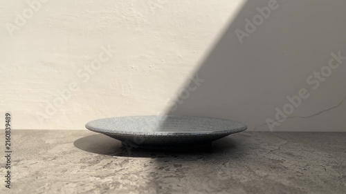 side view of empty grey plate with shadows. gray cement table. white wall. copy space, empty, free, negative, text, design. black, dark. line, lines. sunlight, sunrise, sunshine. product. close up.
