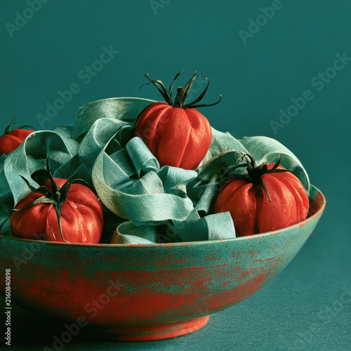 A vibrant bowl overflows with ruby-red tomatoes nestled amongst pale blue ribbons