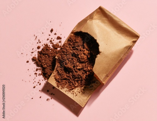 Loose, rich brown powder spills from an open paper bag onto a pink surface