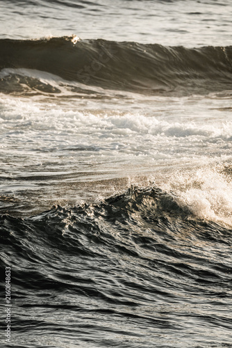 Close-up of rolling ocean waves with textured dark water and warm sunlight reflections on the sea surface