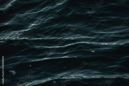 фотографія Close-up of dark, moody ocean surface with rolling ripples and teal reflections