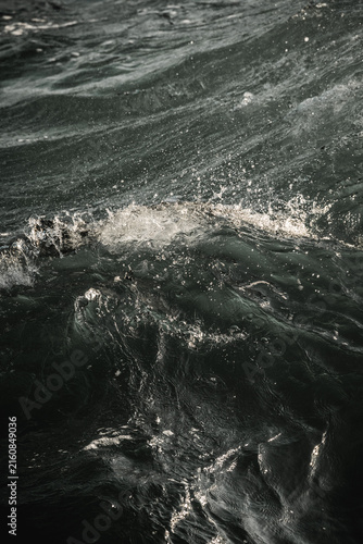 Close-up photograph of dark choppy ocean water with swirling waves, white foam and dramatic surface texture