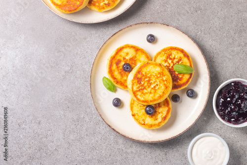 Golden cottage cheese pancakes with sour cream, blueberry jam and fresh berries. Healthy breakfast concept.