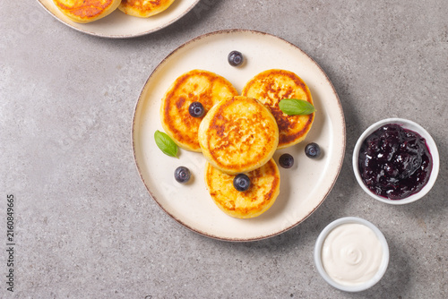 Golden cottage cheese pancakes with sour cream, blueberry jam and fresh berries. Healthy breakfast concept.