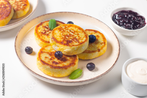Golden cottage cheese pancakes with sour cream, blueberry jam and fresh berries. Healthy breakfast concept.