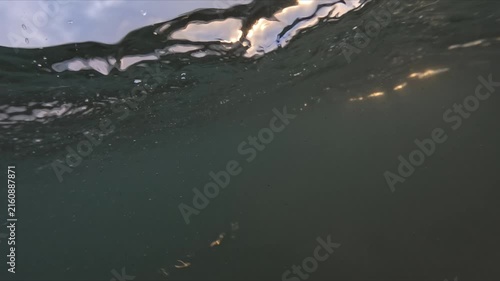 Slow motion sea waves flow across an underwater camera at sunset with golden light illuminating water and bubbles