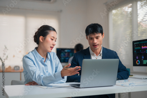 Asian business colleagues collaborating on a laptop in a modern office, analyzing data and discussing financial reports