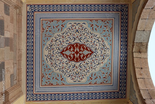 The ceiling of a mosque adorned with traditional Turkish motifs. The decorations, dating back to the Ottoman era, consist of geometric and floral patterns.