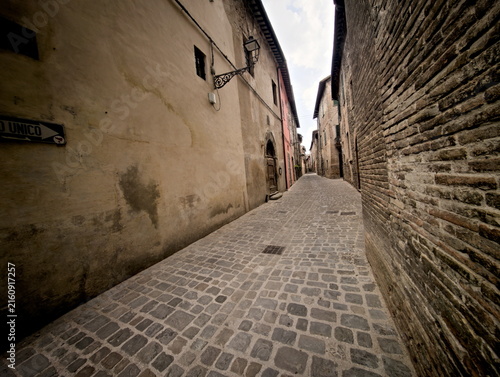 Stretto vicolo medievale a Sant'Angelo in Vado con mura in pietra a vista e pavimentazione in ciottoli.