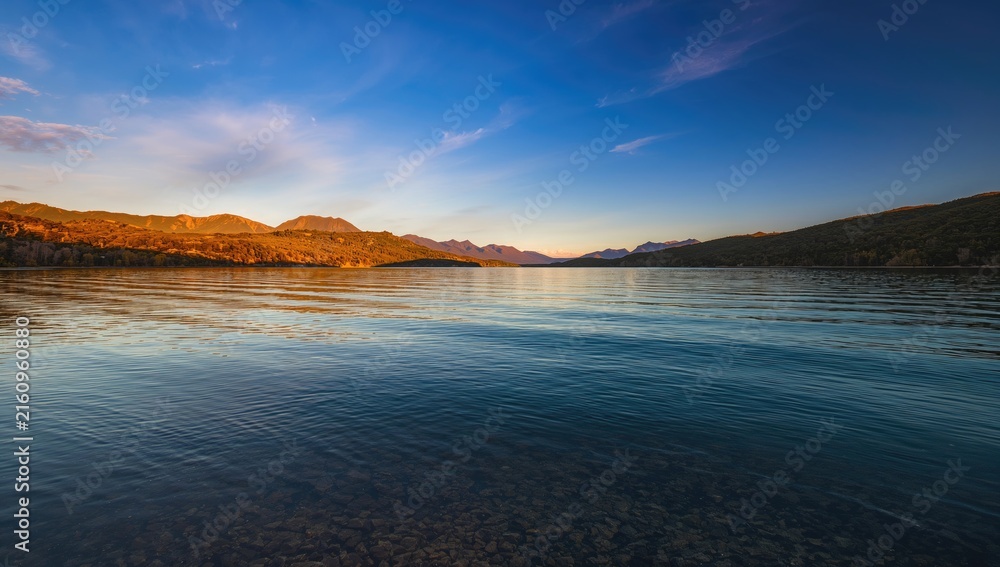 Obraz premium Serene Mountain Lake at Sunrise with Calm Water Reflection and Clear Blue Sky
