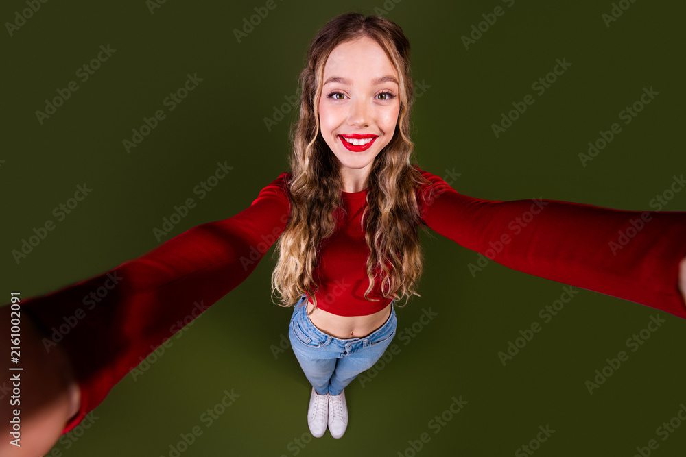 Naklejka premium Young woman in red crop top jeans smiles with outstretched arms against a green background for a bright fashion lifestyle photo