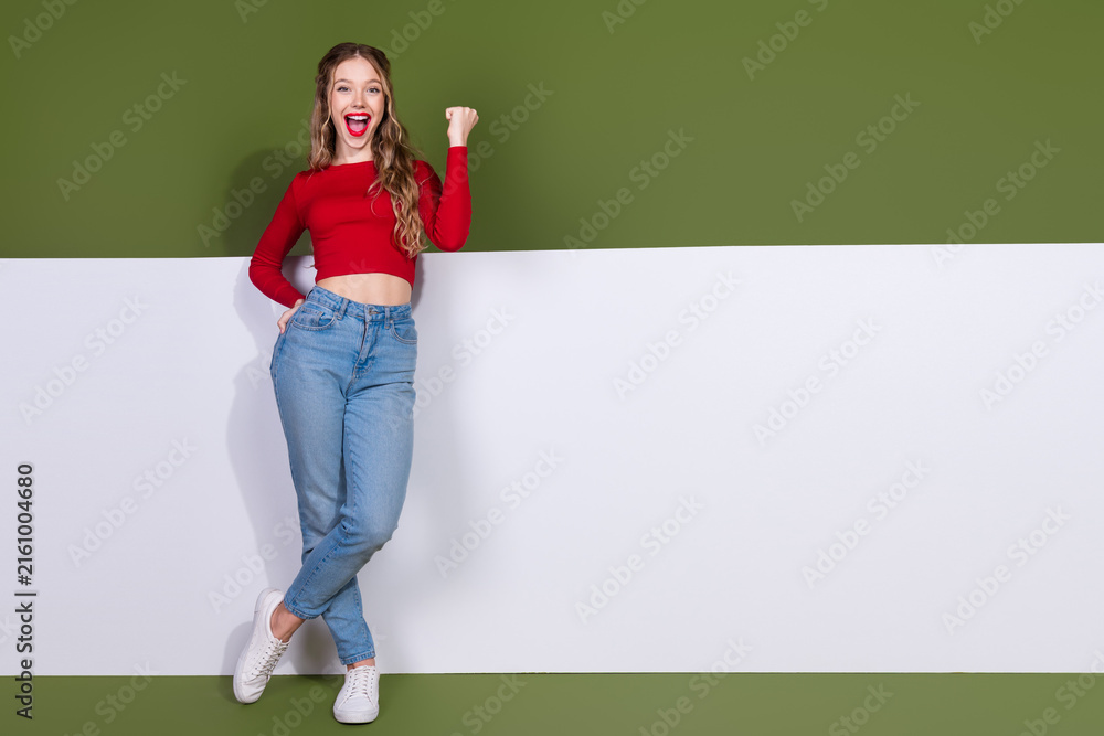 Naklejka premium Young woman in red crop top and jeans smiles and cheers standing against green white backdrop