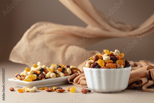 The mix of various nuts and raisins in a white bowl on a beige background.
