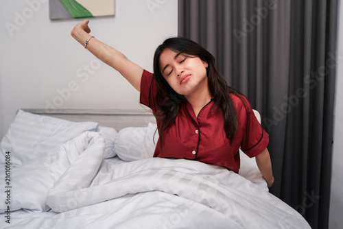Obraz na plátně Beautiful Asian woman waking up from sleep, stretching hands and feeling sleepy in her bedroom