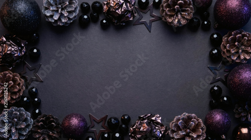 Luxurious Christmas border with dark purple ornaments, glitter pinecones, and stars on dark background, copy space