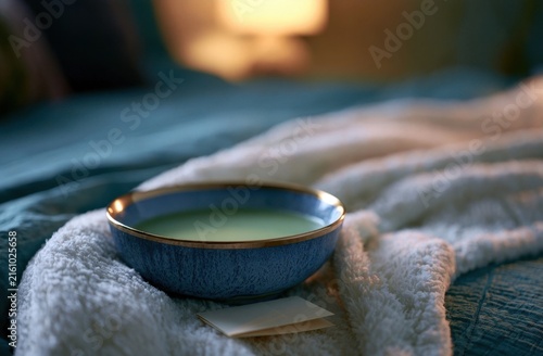 Small ceramic bowl with green tea on a folded blanket in a cozy bedroom setting